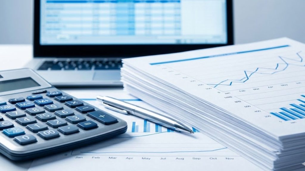 Calculadora, gráficos y documentos financieros frente a una laptop con hojas de cálculo.